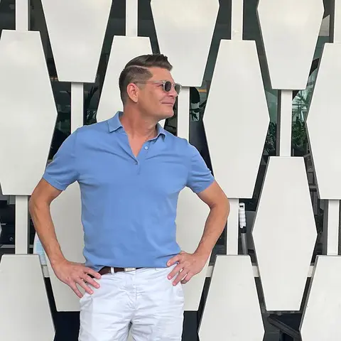 A man in blue shirt and white pants standing next to wall.